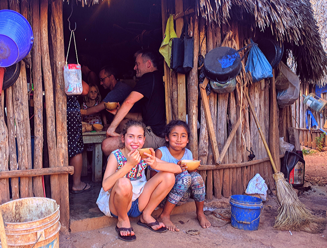 two girls sitting in the doorway of a traditional Mayan home